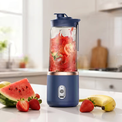 A portable electric blender with a navy blue base and lid, shown blending red fruit in a clear jar. The blender is placed on a kitchen counter with strawberries, a watermelon slice, and a banana nearby.